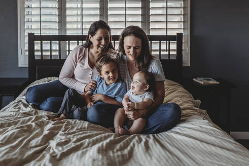 Lachendes gleichgeschlechtliches Paar, das zusammen auf dem Bett der Mutter sitzt - CAVF70092