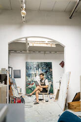 Artist sitting in his studio, using digital tablet - PESF01723