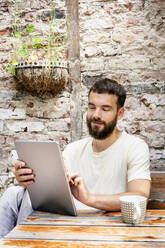 Young man sitting in backyard, using digital tablet - PESF01726