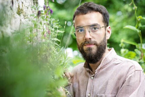 Portrait of young bearded man, standing in garden - PESF01734