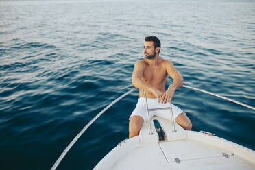 Young man sitting at bow of a boat, watching the sea - MIMFF00026