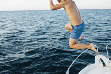 Junger Mann springt von einem Boot ins Meer - MIMFF00028