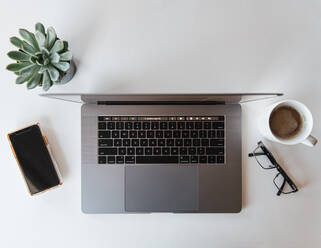 Overhead view of workspace with laptop, phone, glasses and coffee. - CAVF70149