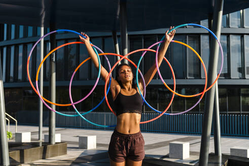 Junge Frau der Generation Z hält fünf Hula-Hoop-Reifen in der Innenstadt bei Sonnenuntergang - CAVF70195