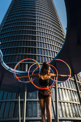 Active young woman holding five Hula Hoop in downtown at sunset - CAVF70196