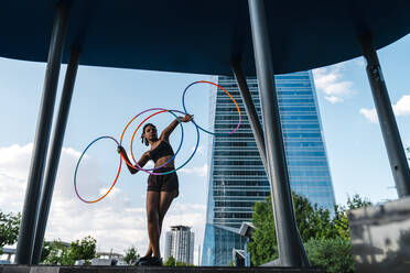 Perspektivische Ansicht einer jungen Frau, die mit vier Hula-Hoop-Reifen in der Stadt tanzt - CAVF70197