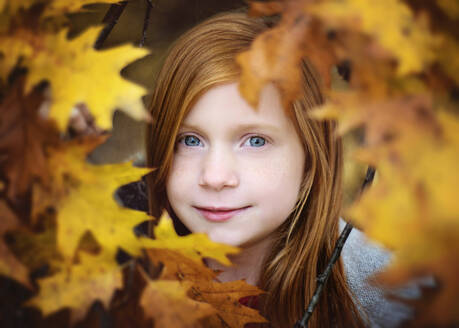 Red Haired Girl Looking Through Yellow Fall Leaves - CAVF70239
