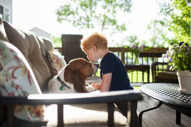 Kleiner Junge küsst seinen Basset Hound auf der Terrasse im Frühling - CAVF70256