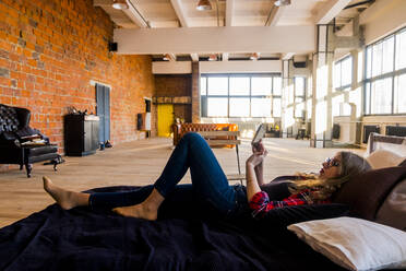 Full length side view of young woman using tablet computer while lying on bed at home - CAVF70292