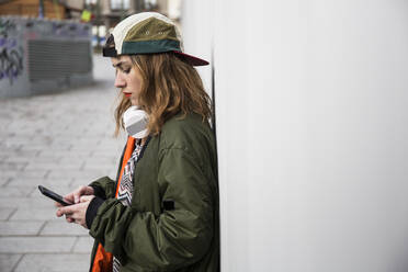 Seitenansicht einer Frau, die ein Smartphone benutzt, während sie an der Wand steht - CAVF70305