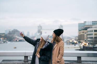 Freunde nehmen Selfie, während stehend gegen Fluss in der Stadt gegen Tower Bridge - CAVF70322