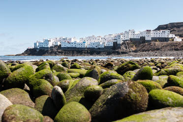 Blick von einem Kieselstrand auf ein weißes Häuserviertel mit Blick auf das Meer - CAVF70333