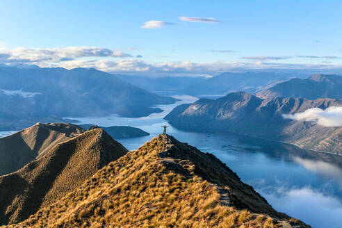 Mann steht auf einem Berggipfel mit Blick auf einen blauen See in Neuseeland. - CAVF70343