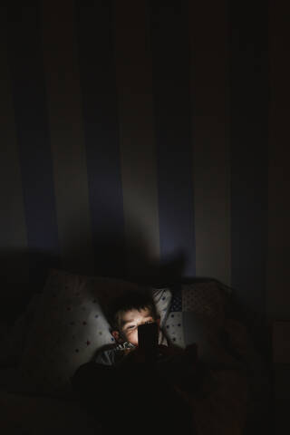 Little boy ying in bed using smartphone at night stock photo