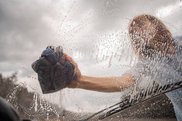 Niedriger Blickwinkel der Frau beim Autowaschen durch die Windschutzscheibe gesehen - CAVF70352