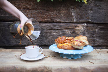 Abgeschnittene Hand eines Teenagers, der Kaffee in eine Tasse gießt, neben Desserts auf dem Tisch - CAVF70370