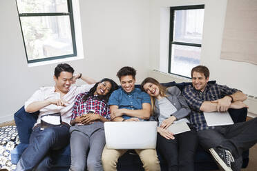 Cheerful business people using laptop while relaxing on sofa in office - CAVF70376