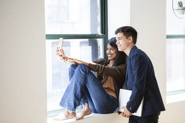 Glückliche Geschäftskollegen machen ein Selfie mit ihrem Smartphone am Fenster in einem kreativen Büro - CAVF70384