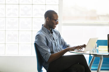 Businessman using laptop on table in creative office - CAVF70393