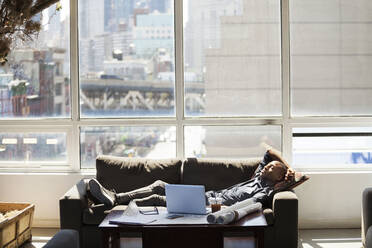 Businessman relaxing on sofa in creative office - CAVF70399