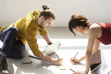 Business people writing in notes on floor at brightly lit creative office - CAVF70400