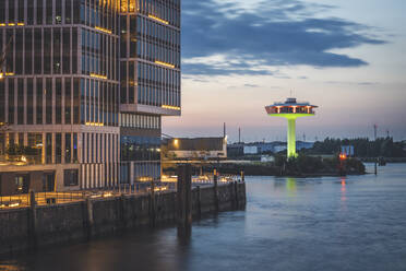 Deutschland, Hamburg, Gebäude am Wasser in der Abenddämmerung mit Leuchtturm Zero im Hintergrund - KEBF01421