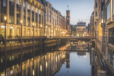 Germany, Hamburg, Street lights illuminating buildings along shiny Elbe river canal at dusk - KEBF01428