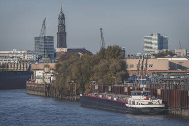 Germany, Hamburg, Container ship moored in harbor with tower of Saint Michaels Church in background - KEBF01448
