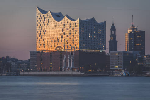 Deutschland, Hamburg, Elbphilharmonie in der Abenddämmerung mit St. Michaelskirche im Hintergrund - KEBF01450
