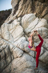 Woman practicing king dancer pose on rocks - CAVF70424