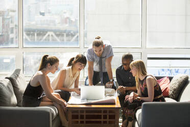 Business people looking at laptop on table in creative office - CAVF70439