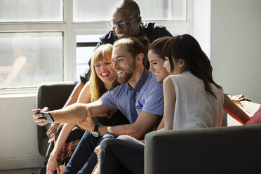 Glückliche Geschäftsleute klicken Selfie auf Sofa in kreativen Büro - CAVF70441