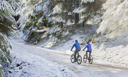 Pärchen beim Mountainbiken im verschneiten Wald - HOXF04423