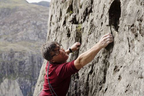Fokussierter männlicher Kletterer beim Erklimmen einer Felswand - HOXF04483