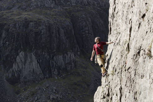 Männlicher Bergsteiger, der eine hohe Felswand erklimmt und über die Schulter blickt - HOXF04492
