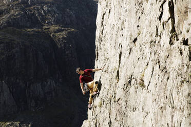 Männlicher Bergsteiger, der eine große Felswand erklimmt und über die Schulter nach unten schaut - HOXF04495