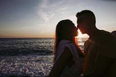 Junges Paar, das sich bei Sonnenuntergang am Strand küsst - LJF01093