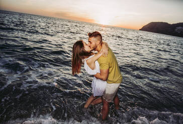 Young couple kissing each other at the beach during sunset - LJF01098