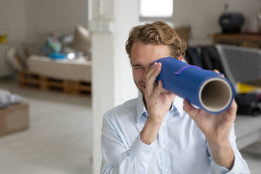 Young businessman in his office, looking through blue pipe - MOEF02699