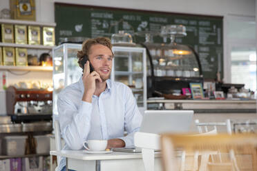 Junger Geschäftsmann telefoniert in einem Cafe - MOEF02701