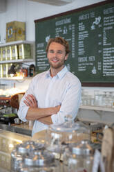 Young businessman in a cafe, with crossed arms behind counter - MOEF02705