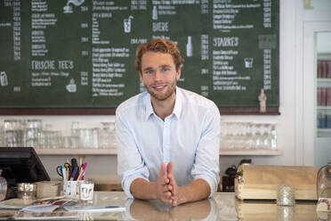 Junger Geschäftsmann in einem Café, an den Tresen gelehnt - MOEF02706