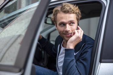 Young man phoning and sitting in car, looking sideways - MOEF02709