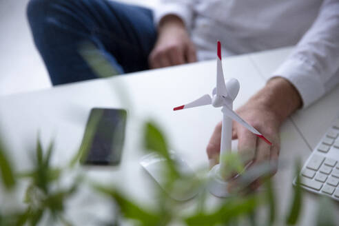 Close-up of man with hand on wind turbine model on table - MOEF02712