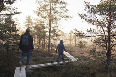 Vater und Sohn gehen auf Brettern im Wald, Finnland - CUF53547