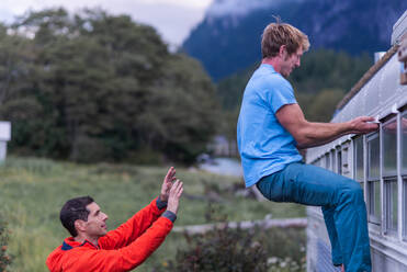 Mann beobachtet den Rücken eines Freundes, der auf ein Wohnmobil klettert, Squamish, British Columbia, Kanada - CUF53562