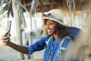 Happy young female backpacker taking selfie with camera phone - HOXF04530