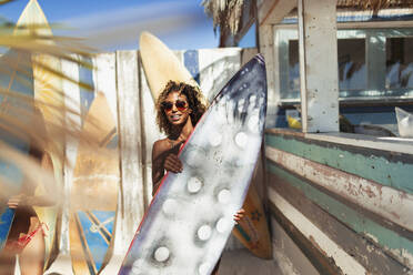 Portrait junge Frau mit Surfbrett am sonnigen Strand - HOXF04531