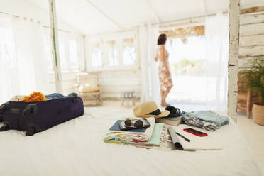 Woman standing in beach hut doorway beyond suitcase and belongings on bed - HOXF04540