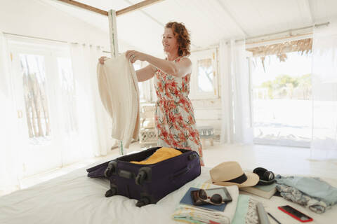 Frau beim Auspacken des Koffers im Schlafzimmer einer Strandhütte, lizenzfreies Stockfoto